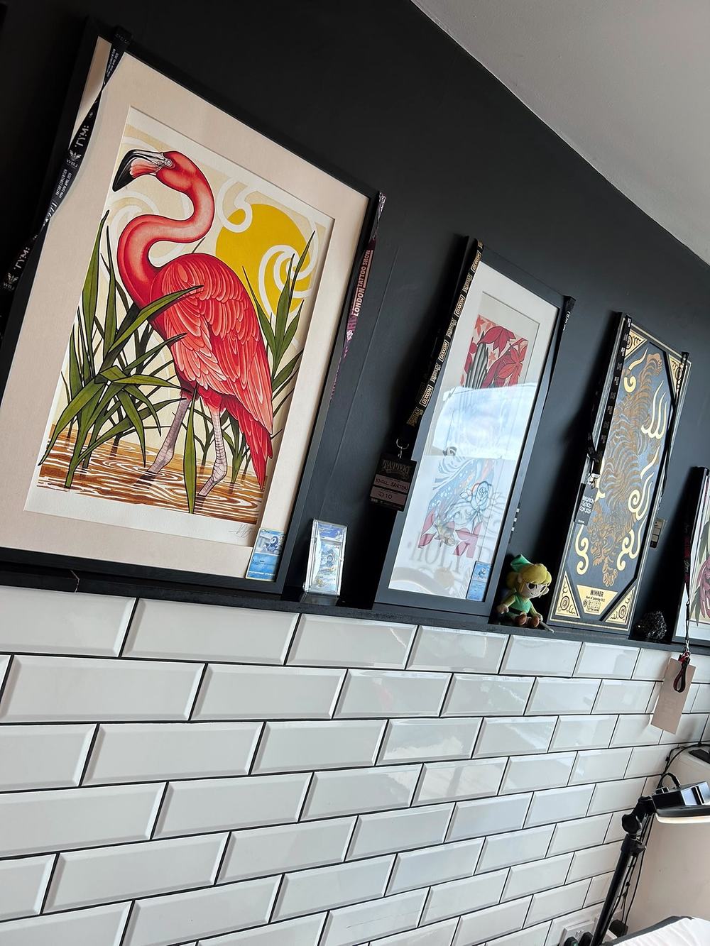 Framed artwork above white tiles, with a flamingo painting